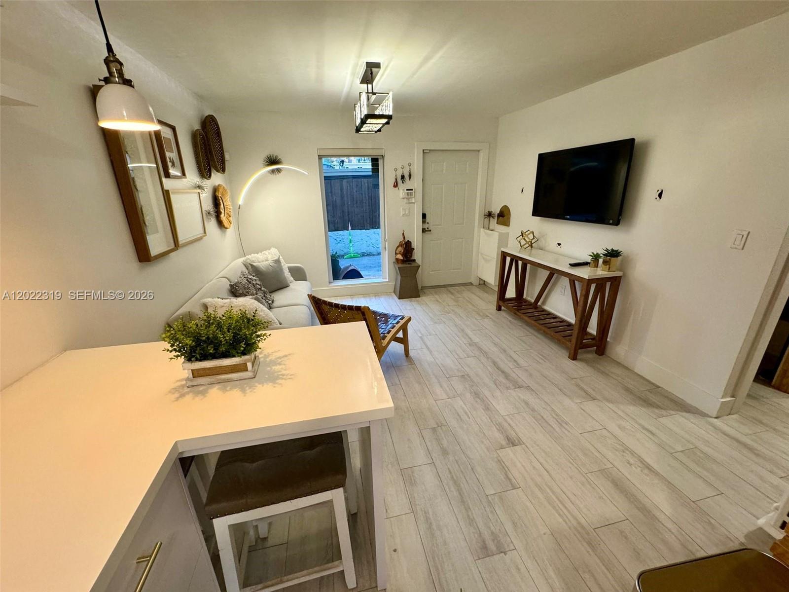 A living room features light wood-look tile flooring, a mounted television, and a white sofa — 1121 SW 7th St # 1, Miami FL 33130, MIAMI, FL