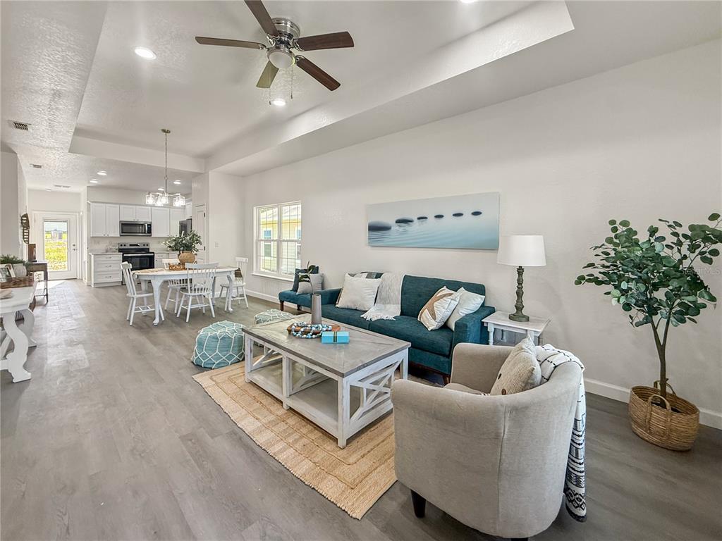 An open-concept living and dining area features light wood-look flooring and a teal sofa — 15341 NW 135TH TERRACE, ALACHUA, FL