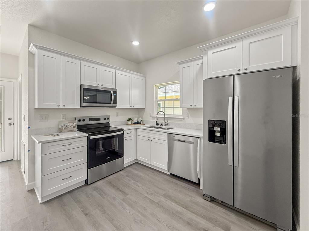 A kitchen features white cabinets, stainless steel appliances, and light wood-look flooring — 15341 NW 135TH TERRACE, ALACHUA, FL