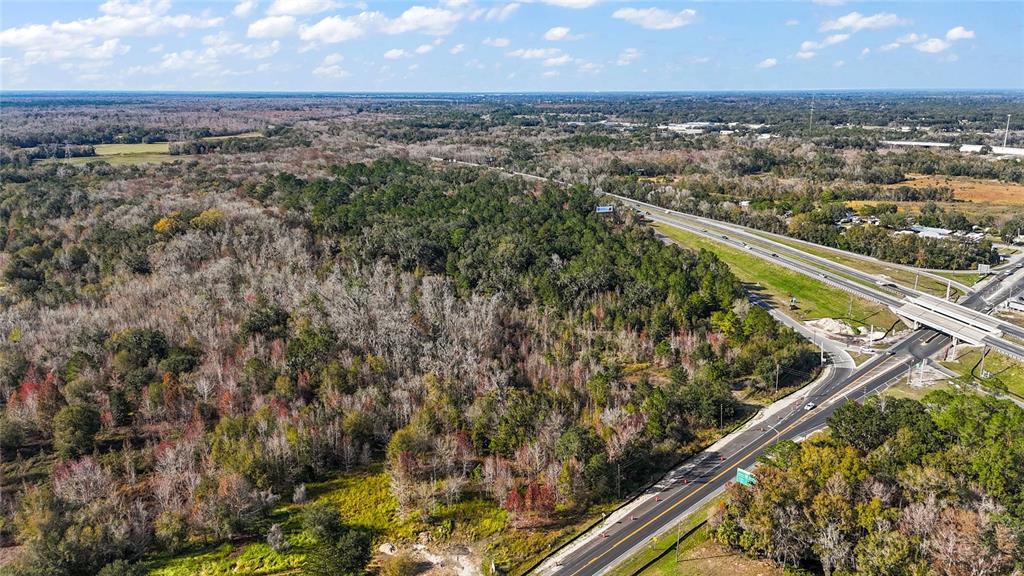 An aerial view shows a wooded lot adjacent to a highway overpass and paved road — HWY 301 / MAIN STREET, WILDWOOD, FL