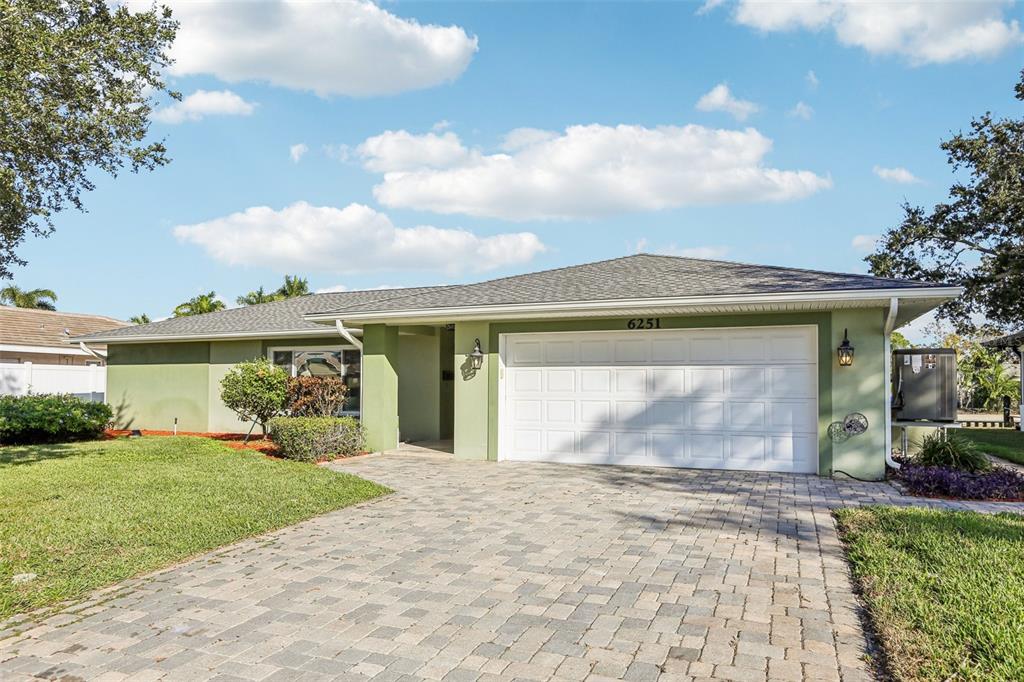 A single-story house with a green exterior, a white garage door, and a paver driveway — 6251 18TH STREET NE, ST PETERSBURG, FL