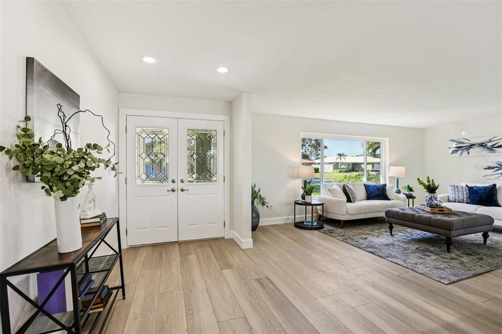 A bright entryway with light wood flooring leads into a living room with a sofa — 6251 18TH STREET NE, ST PETERSBURG, FL