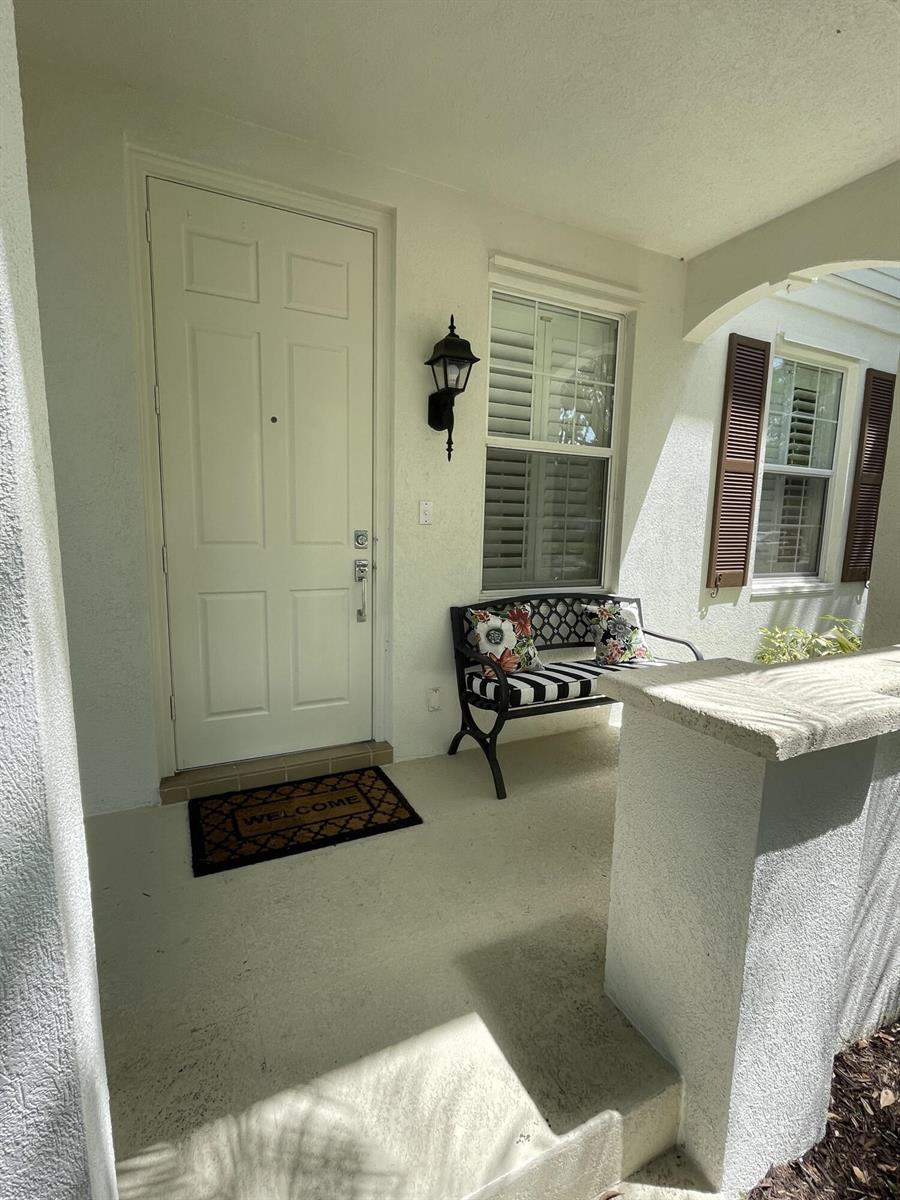 A front porch features a white door, a window with shutters, and a metal bench — 2857 E Community Drive, Jupiter FL 33458, JUPITER, FL
