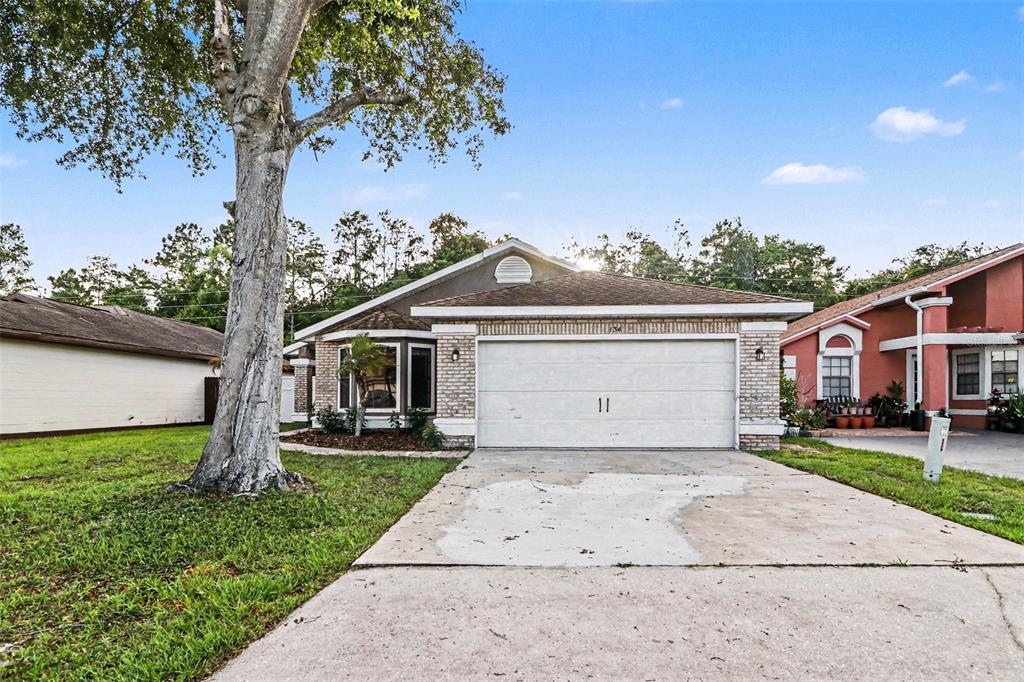 A single-story house with a white garage door, brick facade, and a large front tree — 134 CORALWOOD CIRCLE, KISSIMMEE, FL