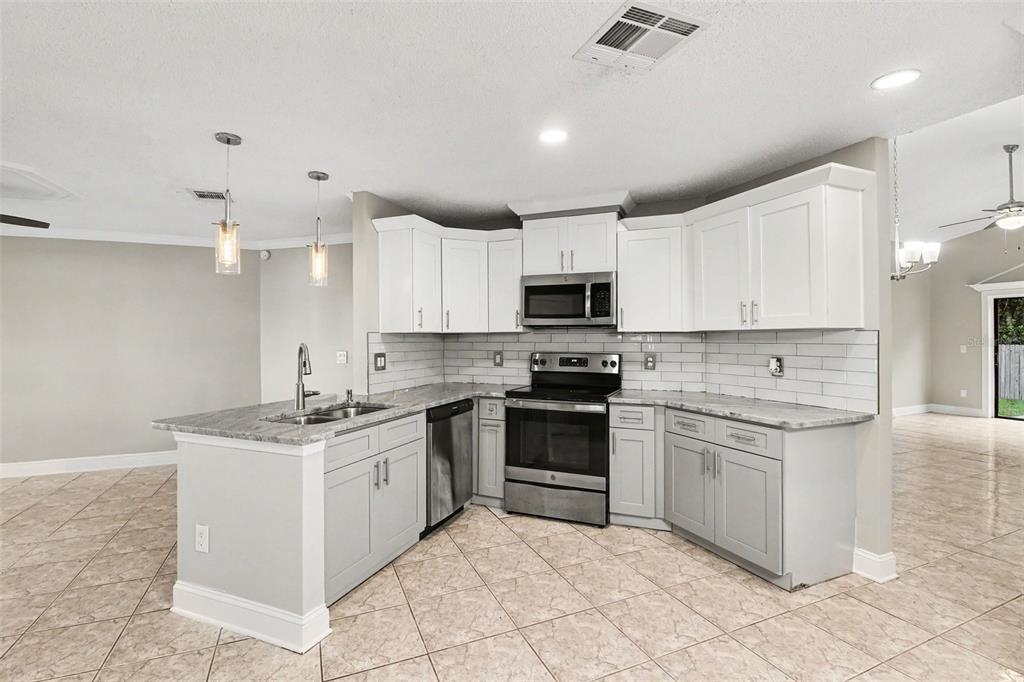 A kitchen features white upper cabinets, gray lower cabinets, stainless steel appliances, and tile flooring — 134 CORALWOOD CIRCLE, KISSIMMEE, FL