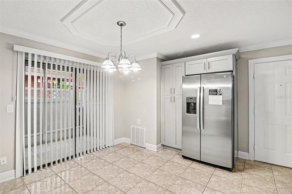 A dining area features tile flooring, a chandelier, a stainless steel refrigerator, and vertical blinds — 134 CORALWOOD CIRCLE, KISSIMMEE, FL