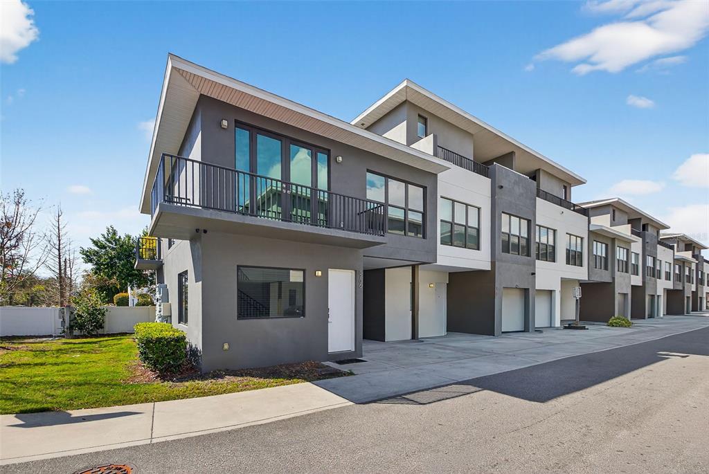 A modern multi-story townhouse with a gray and white exterior, balconies, and attached garages — 8706 PALM RANCHES PLACE, TAMPA, FL