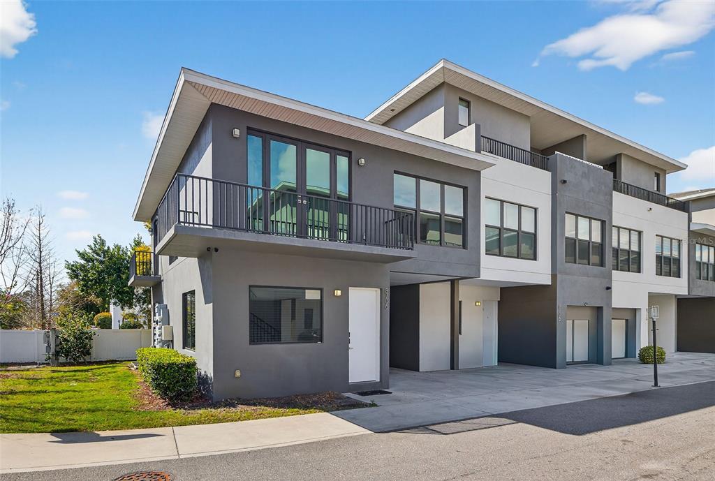 A modern multi-story townhouse with a gray and white exterior, balconies, and a concrete driveway — 8706 PALM RANCHES PLACE, TAMPA, FL