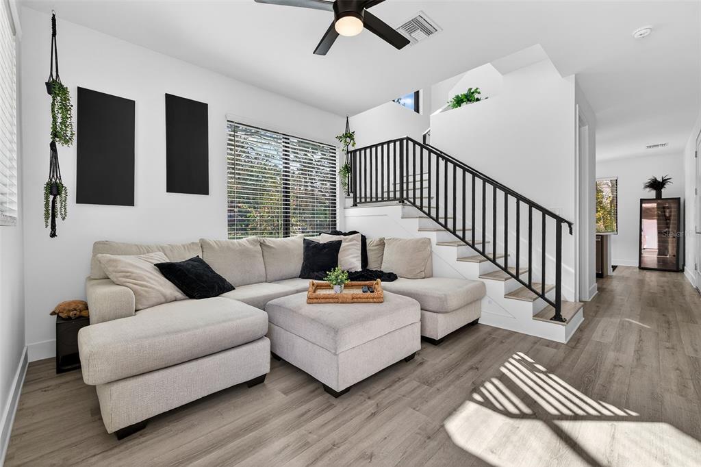 A living room features a beige sectional sofa, a staircase with black railings, and wood-look flooring — 8706 PALM RANCHES PLACE, TAMPA, FL