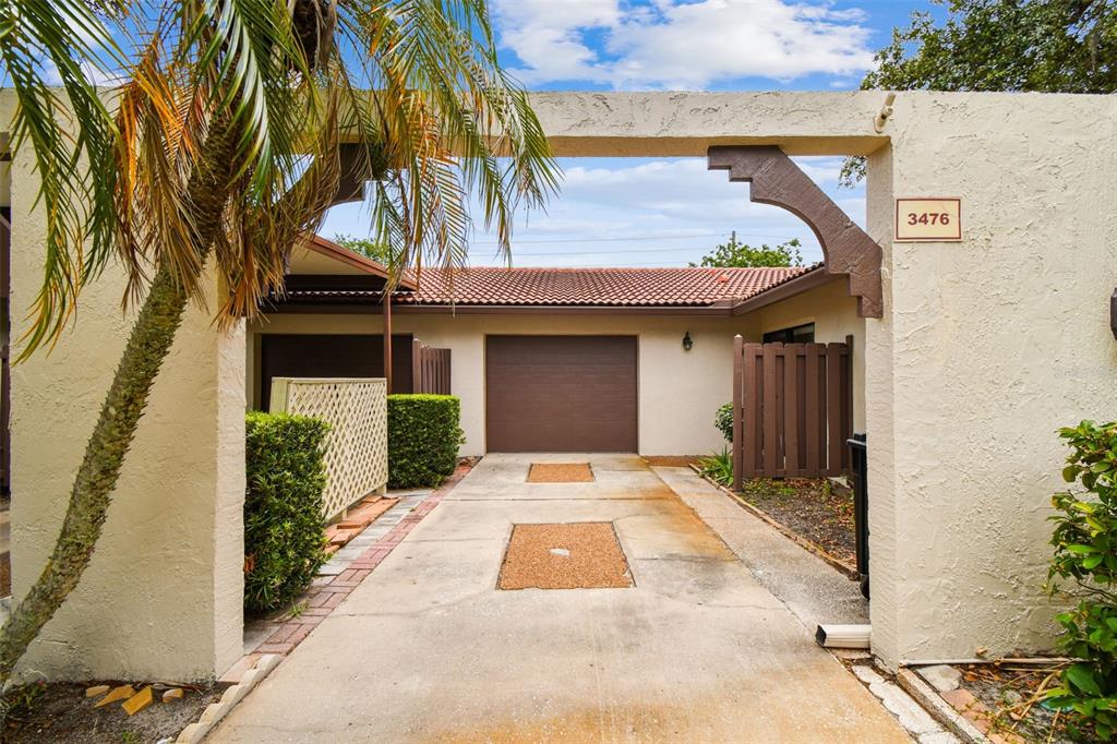 A concrete driveway leads to a single-car garage framed by a stucco archway and palm tree — 3476 TARPON WOODS BOULEVARD, PALM HARBOR, FL
