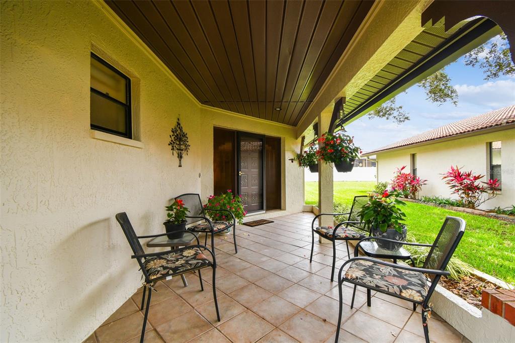 A covered patio features tile flooring, outdoor seating, and hanging flower baskets near a front door — 3476 TARPON WOODS BOULEVARD, PALM HARBOR, FL
