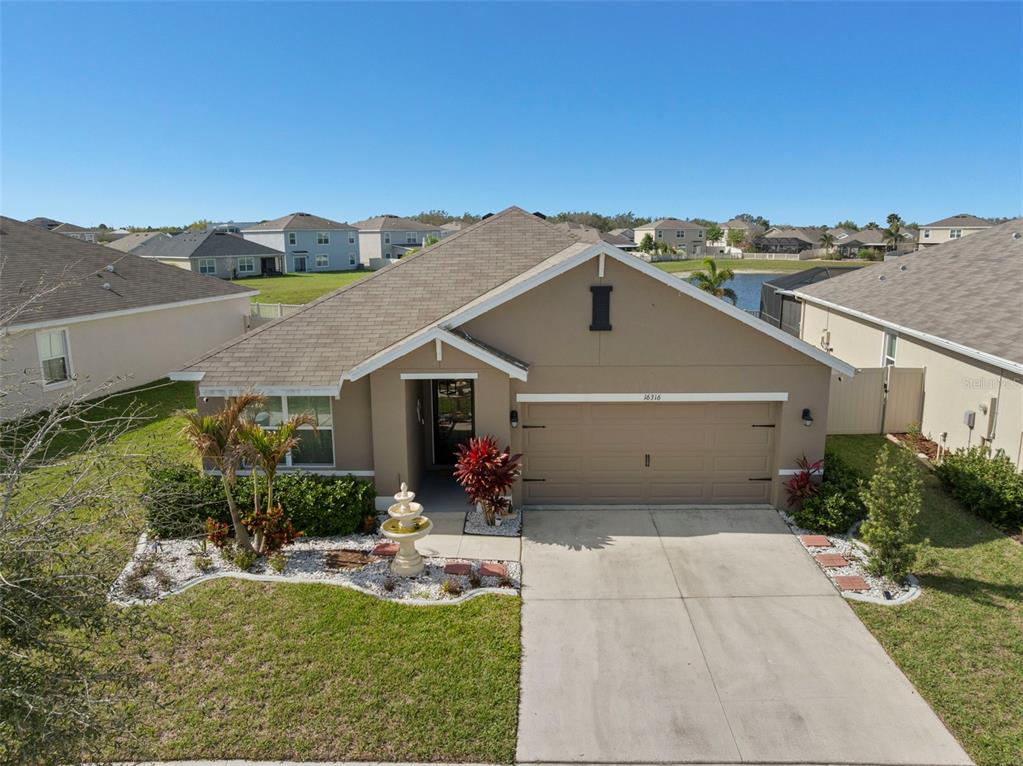 A single-story suburban house with a tan stucco exterior, a two-car garage, and a fountain — 16316 LITTLE GARDEN DRIVE, WIMAUMA, FL