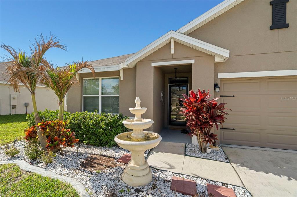 A tan house exterior features a front fountain, palm tree, and a single-car garage — 16316 LITTLE GARDEN DRIVE, WIMAUMA, FL