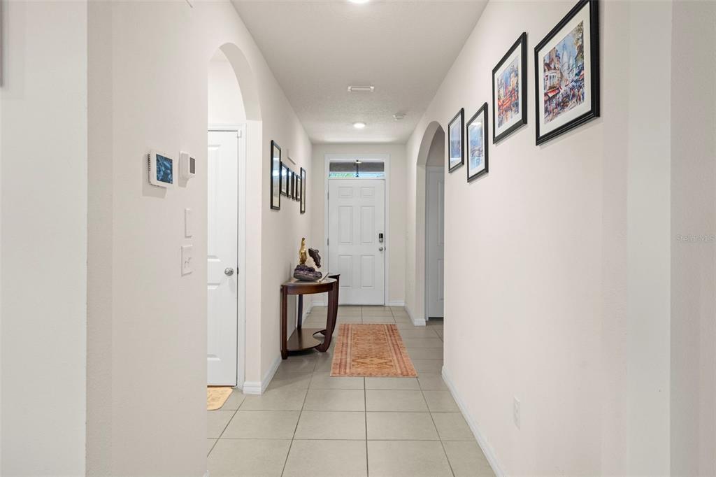 A tiled entryway features a white front door, a console table, and framed wall art — 16316 LITTLE GARDEN DRIVE, WIMAUMA, FL