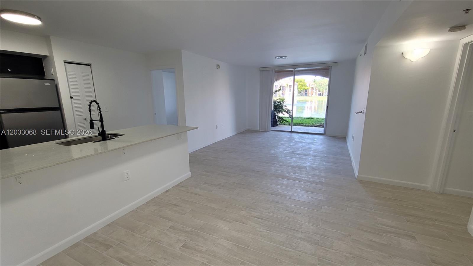 An open-concept living area features light wood-look tile flooring and a kitchen with a breakfast bar — 2021 Renaissance Blvd # 104, Miramar FL 33025, MIRAMAR, FL