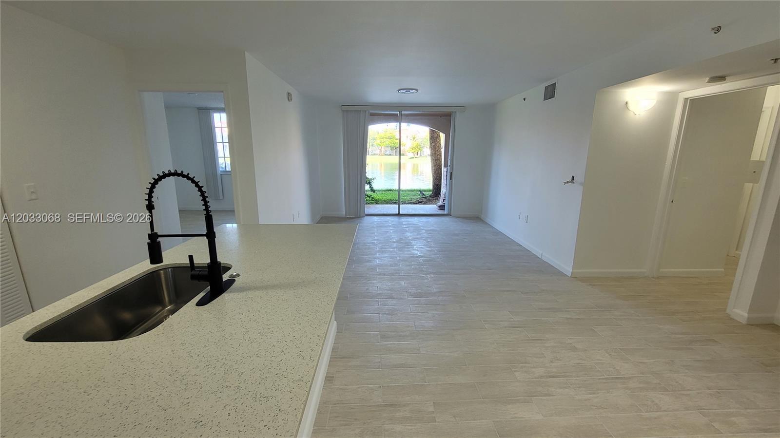An open-concept kitchen and living area features light tile flooring and a sliding glass door — 2021 Renaissance Blvd # 104, Miramar FL 33025, MIRAMAR, FL