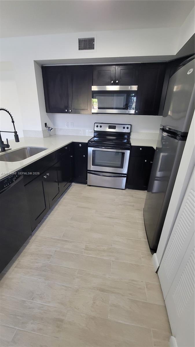 This kitchen features dark cabinetry, stainless steel appliances, and light-colored tile flooring — 2021 Renaissance Blvd # 104, Miramar FL 33025, MIRAMAR, FL