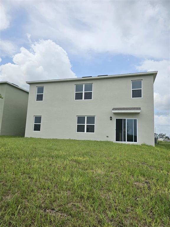 The exterior of a two-story house features light-colored stucco, multiple windows, and a sliding glass door — 3886 WHITNEY WAY, HAINES CITY, FL