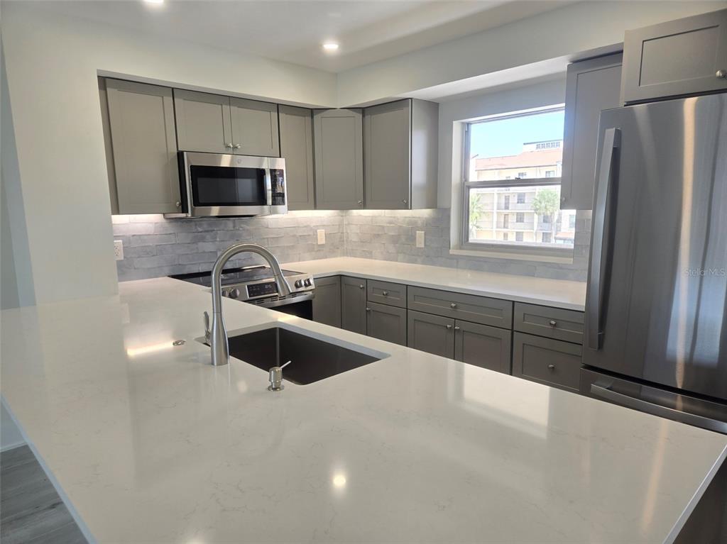 A kitchen features gray cabinets, white countertops, a stainless steel refrigerator, and a tile backsplash — 1300 N PORTOFINO DRIVE UNIT 406, SARASOTA, FL