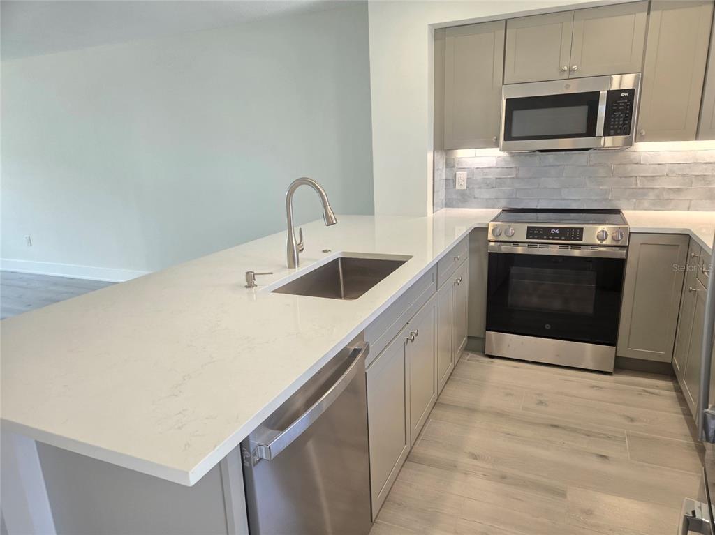 A modern kitchen features gray cabinets, stainless steel appliances, and a white quartz island countertop — 1300 N PORTOFINO DRIVE UNIT 406, SARASOTA, FL