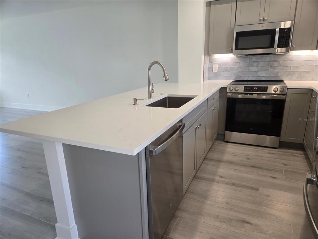 A modern kitchen features a white quartz island, stainless steel appliances, and gray cabinetry — 1300 N PORTOFINO DRIVE UNIT 406, SARASOTA, FL