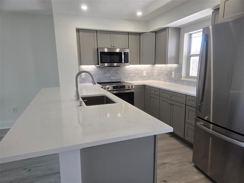A modern kitchen features gray cabinets, white countertops, stainless steel appliances, and a breakfast bar — 1300 N PORTOFINO DRIVE UNIT 406, SARASOTA, FL