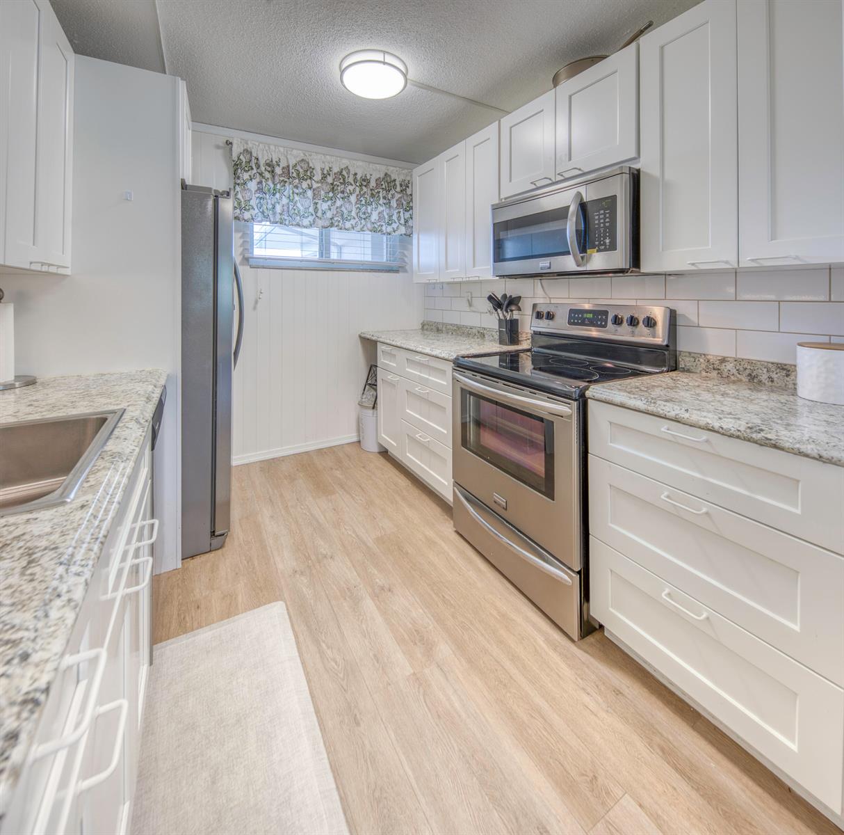 A galley kitchen features white cabinets, stainless steel appliances, granite countertops, and light wood flooring — 2566 Garden Drive S, FL 33461, FL
