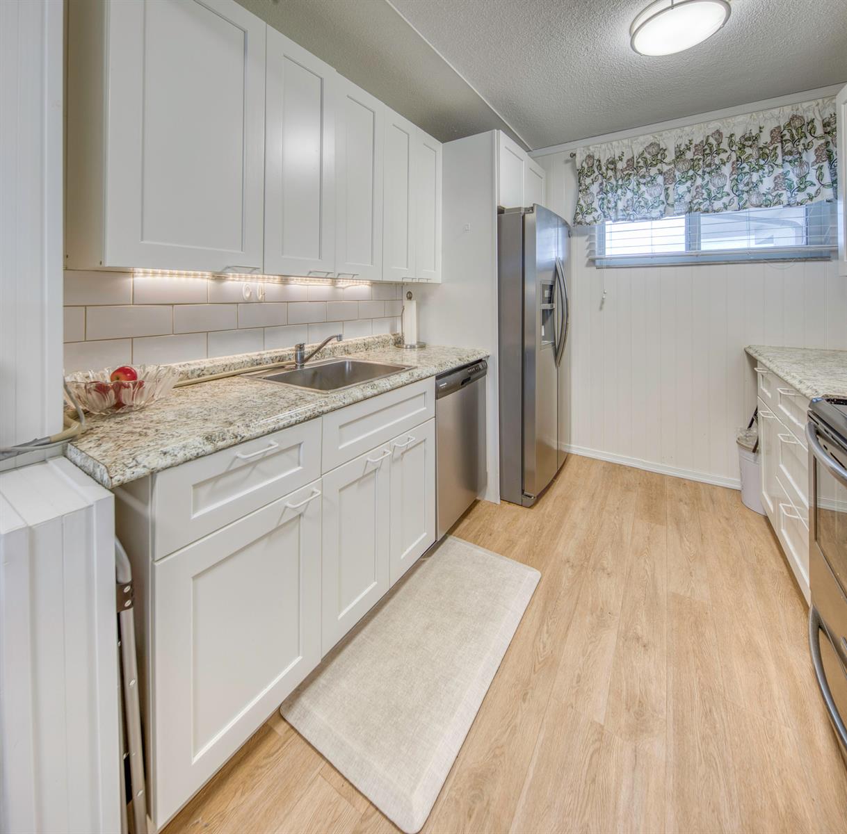 A kitchen features white cabinets, granite countertops, stainless steel appliances, and light wood flooring — 2566 Garden Drive S, FL 33461, FL