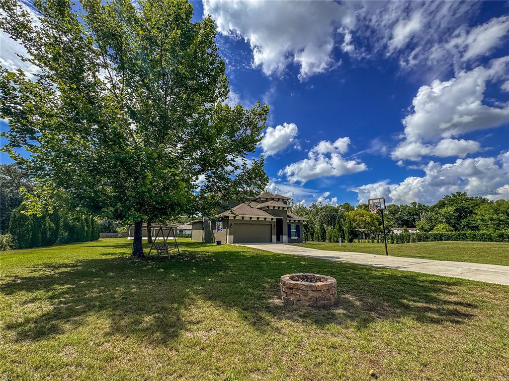 A stone fire pit sits on a grassy lawn in front of a suburban house — 5533 TOWER ROAD, LAND O LAKES, FL