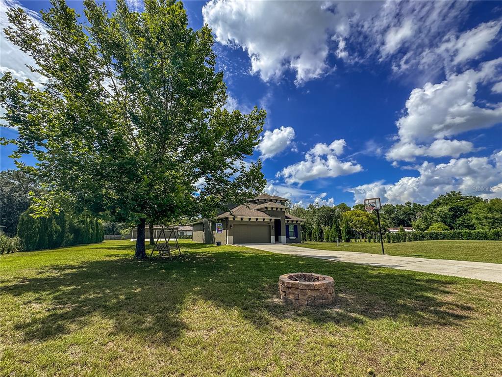 A single-story house with a garage, a large tree, and a fire pit in the yard — 5533 TOWER ROAD, LAND O LAKES, FL