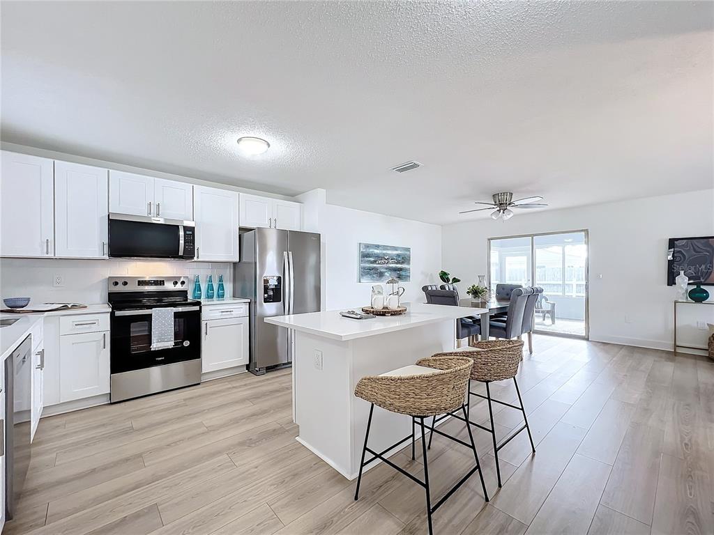 A modern kitchen features white cabinets, stainless steel appliances, a central island, and wood-look flooring — 3932 ASHWOOD LANE UNIT 42, SARASOTA, FL