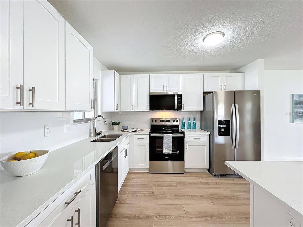 A kitchen features white cabinets, stainless steel appliances, and light wood-look flooring — 3932 ASHWOOD LANE UNIT 42, SARASOTA, FL