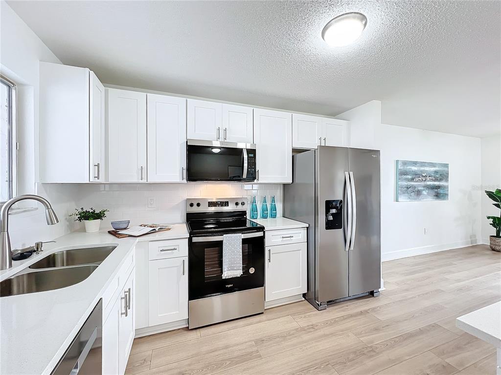 A kitchen features white cabinets, stainless steel appliances, a double sink, and light wood flooring — 3932 ASHWOOD LANE UNIT 42, SARASOTA, FL