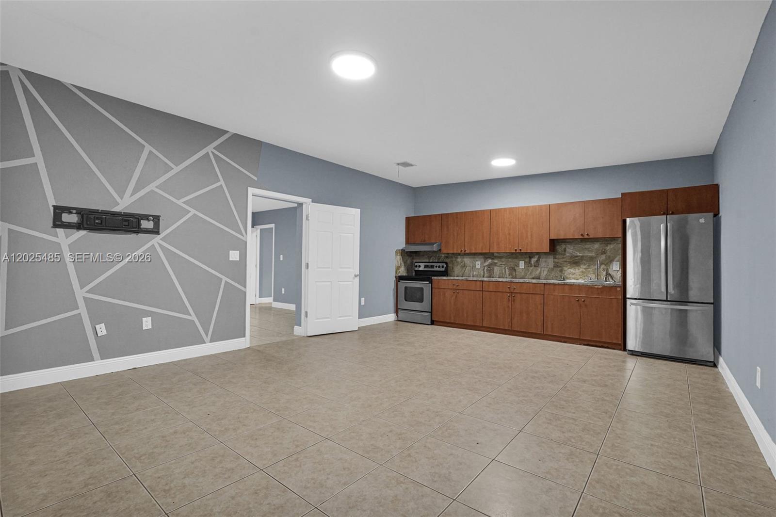 This room features a kitchen area with wood cabinets, stainless appliances, and a geometric accent wall — 14500 NE 2nd Ave # 1, Miami FL 33161, MIAMI, FL