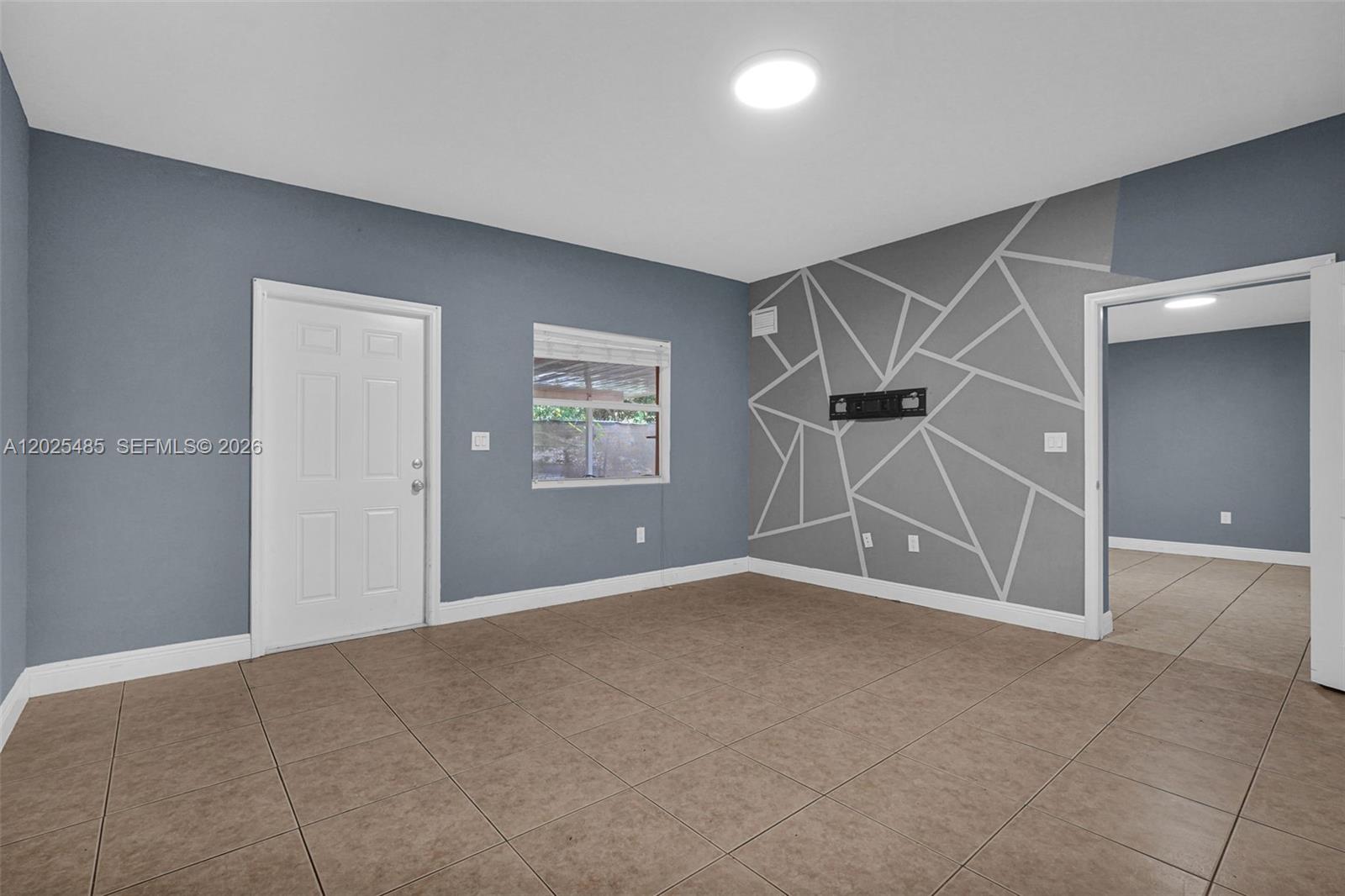 A room with blue walls, tile flooring, and a geometric accent wall with a TV mount — 14500 NE 2nd Ave # 1, Miami FL 33161, MIAMI, FL