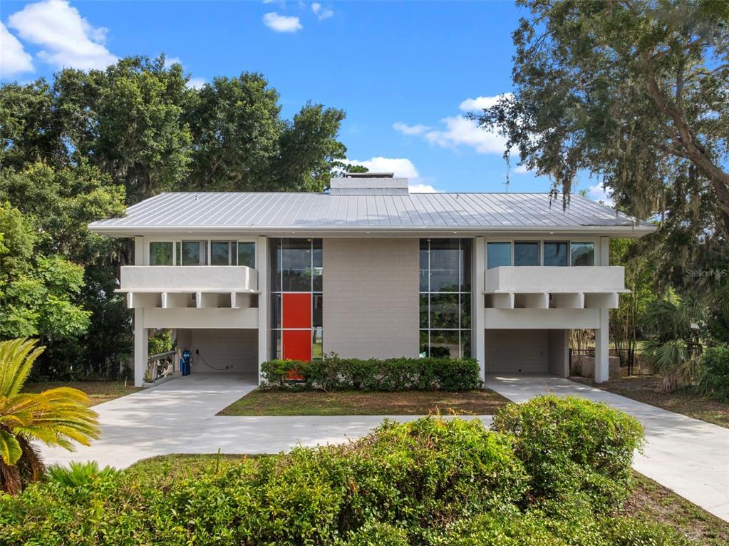 A modern patio with lounge furniture overlooks a swimming pool and a lake with trees — 1540 N LAKE MIRROR DRIVE NW, WINTER HAVEN, FL