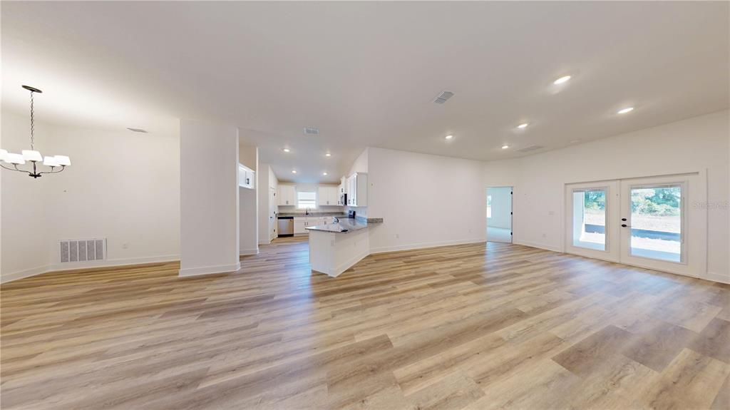 An open-concept living area features light wood-look flooring, recessed lighting, and a kitchen with white cabinetry — 16913 NW 176TH WAY, ALACHUA, FL