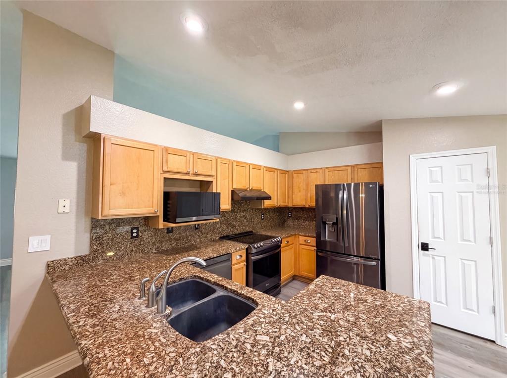 A kitchen features light wood cabinets, granite countertops, a double sink, and stainless steel appliances — 38 HEMLOCK TERRACE PASS, OCALA, FL