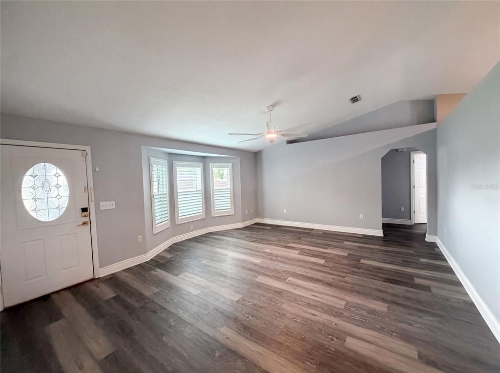 An empty living room features gray walls, wood-look flooring, a ceiling fan, and bay windows — 38 HEMLOCK TERRACE PASS, OCALA, FL