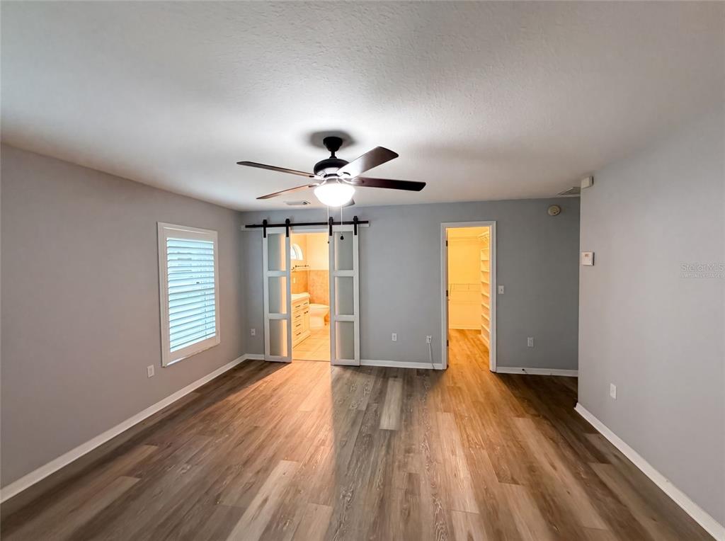 A bedroom with wood-look flooring, a ceiling fan, sliding barn doors, and an attached closet — 38 HEMLOCK TERRACE PASS, OCALA, FL
