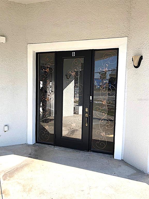 A black front door with glass panels and decorative metal scrollwork sits in a stucco wall — 3001 MICHIGAN AVENUE UNIT B, KISSIMMEE, FL