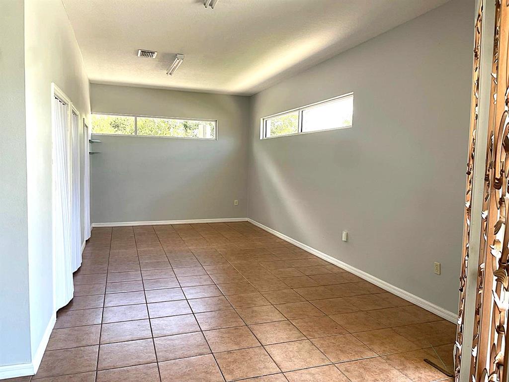 An empty room features light gray walls, tile flooring, and high horizontal windows — 3001 MICHIGAN AVENUE UNIT B, KISSIMMEE, FL