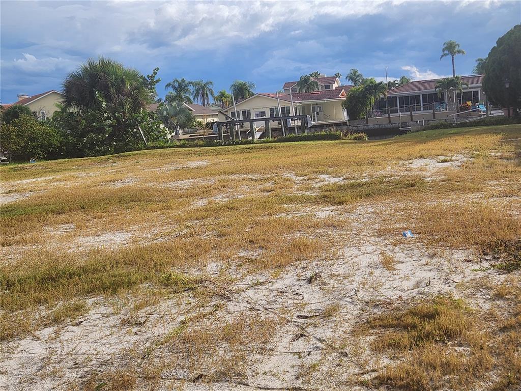 A vacant, sandy lot with sparse grass sits in front of waterfront houses — 3532 FLORAMAR TERRACE, NEW PORT RICHEY, FL