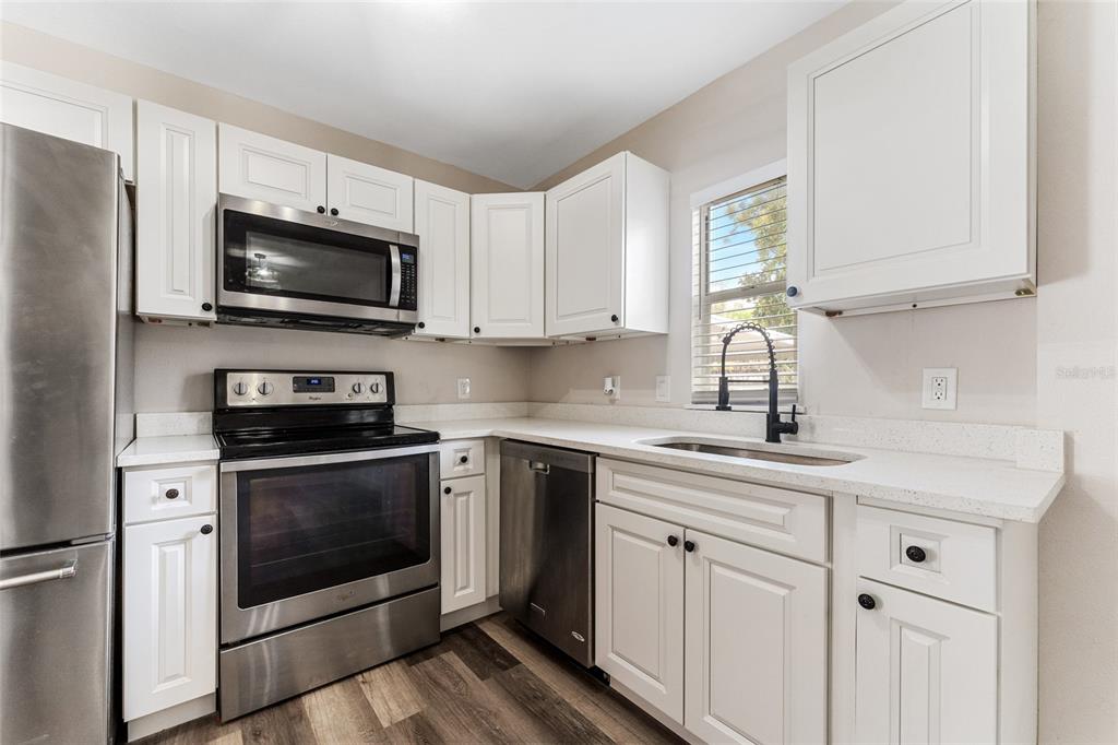 A kitchen features white cabinets, stainless steel appliances, a sink, and wood-look flooring — 1922 23RD STREET S, ST PETERSBURG, FL