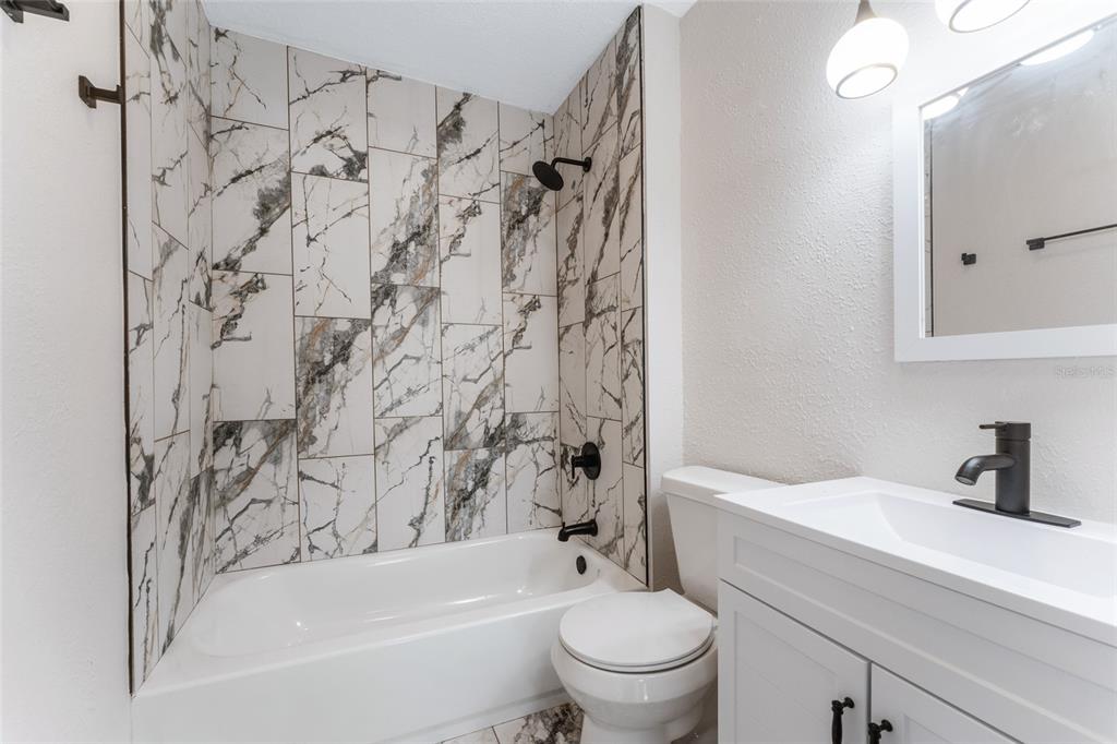 A bathroom features a white vanity, a toilet, and a bathtub with marble-patterned tile walls — 1922 23RD STREET S, ST PETERSBURG, FL