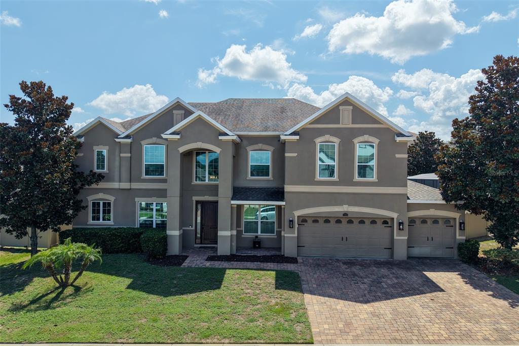 A two-story suburban house with a stucco exterior, a brick driveway, and a three-car garage — 16004 OLLIVETT STREET, WINTER GARDEN, FL