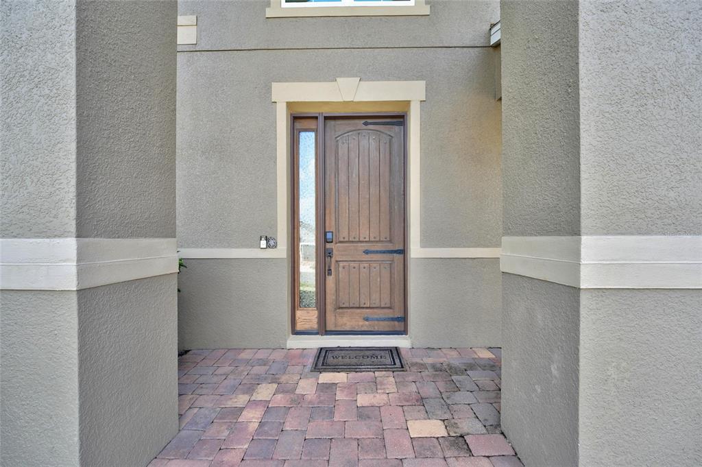 A wooden front door with a side window sits under a covered entryway with pavers — 16004 OLLIVETT STREET, WINTER GARDEN, FL