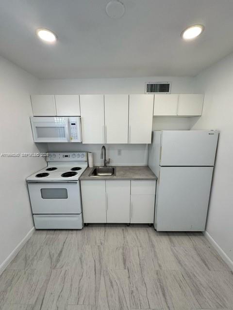 A small kitchen features white cabinets, a white stove, a microwave, and a white refrigerator — 30 SE 4th Ave # 109, Hallandale Beach FL 33009, HALLANDALE BEACH, FL