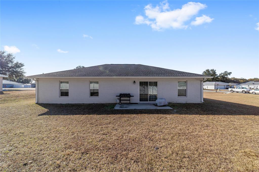 The rear exterior of a single-story house features a concrete patio and a grassy yard — 1803 NE 161ST PLACE, CITRA, FL