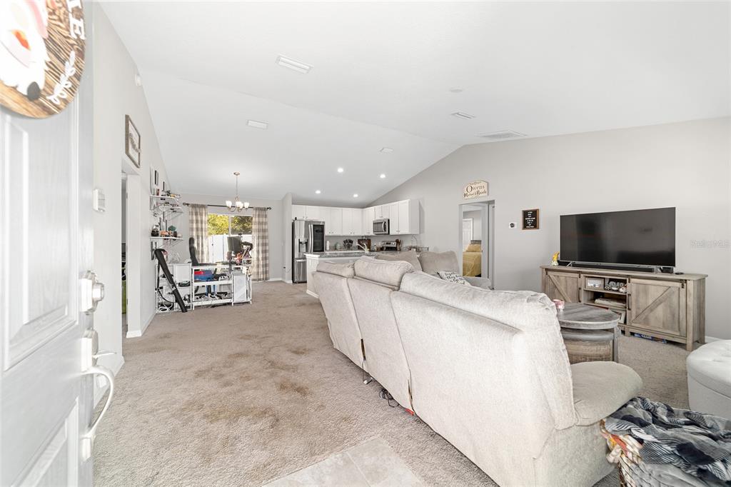 An open-concept living room features a beige sectional sofa, carpeted floors, and a kitchen beyond — 1803 NE 161ST PLACE, CITRA, FL